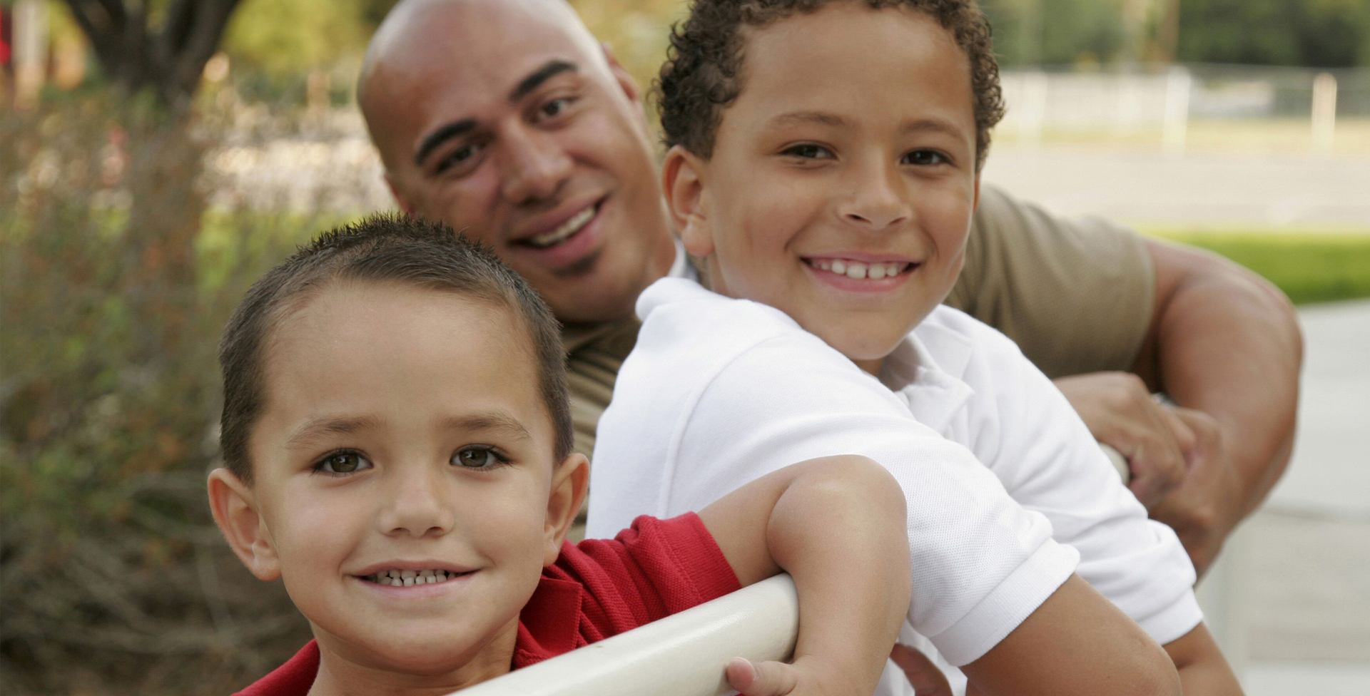 a dad and his tow sons leaning on a rail smiling at the camera